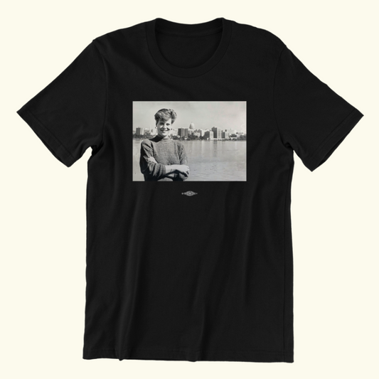 Unisex short-sleeved t-shirt in black. The style is minimalist with a black-and-white throwback photo of Senator Tammy Baldwin in her twenties, arms crossed and the Wisconsin State Capitol in the distance.