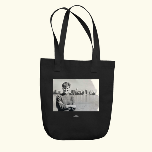 A black tote bag with a black-and-white throwback photo of Senator Tammy Baldwin in her twenties, arms crossed and the Wisconsin State Capitol in the distance.